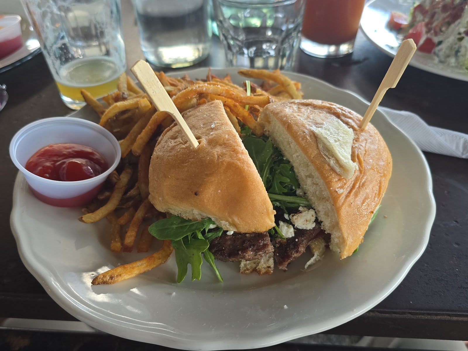 Toasted sandwich with greens and fries on a plate beside drinks