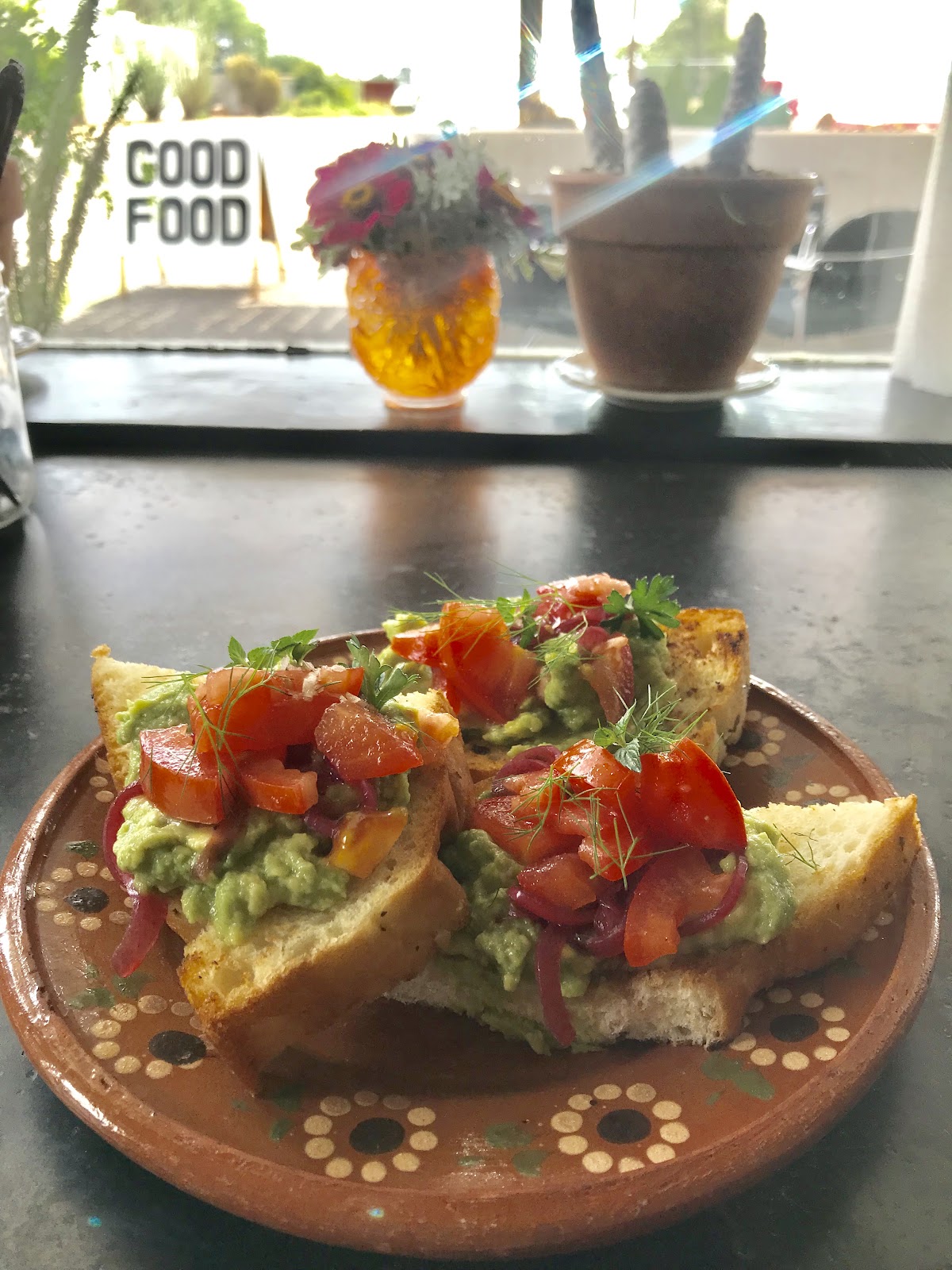 Toasted bread topped with green spread, tomato, red onion, and herbs on a patterned plate